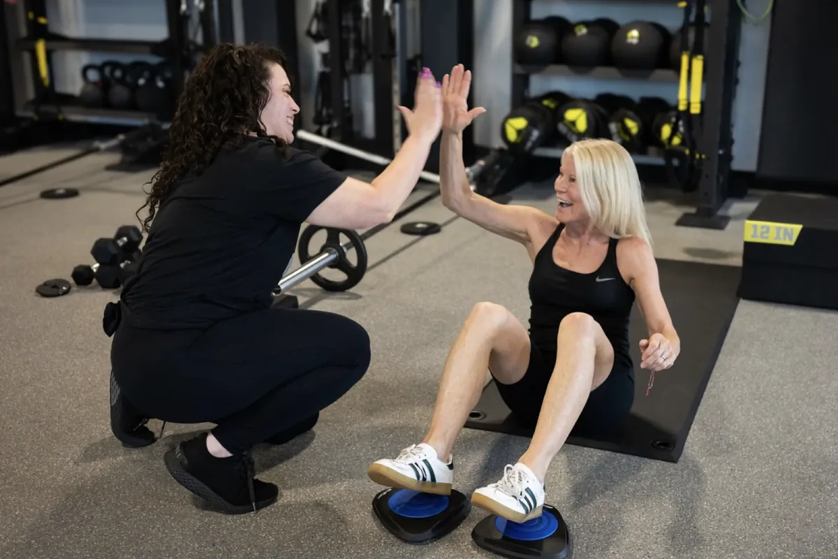 A coach high-fives a member mid core exercise on slider discs