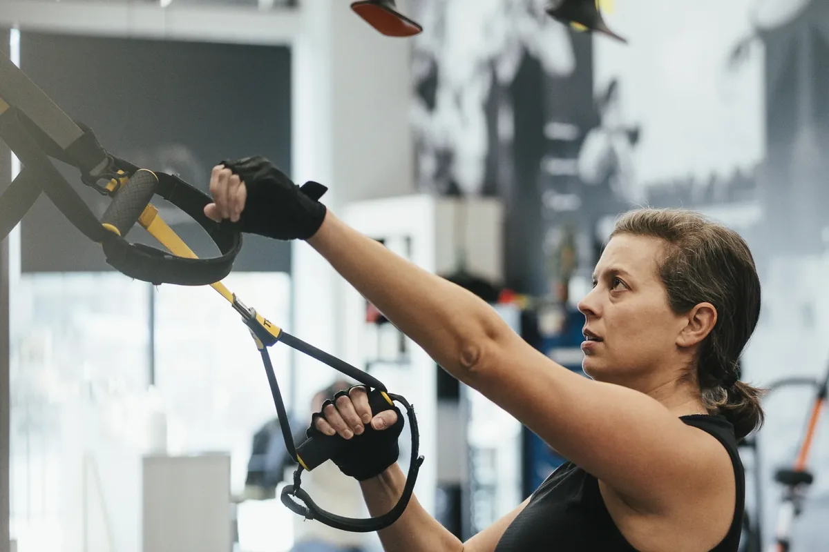 A woman pulls into TRX suspension straps with focus at an Alloy Personal Training studio