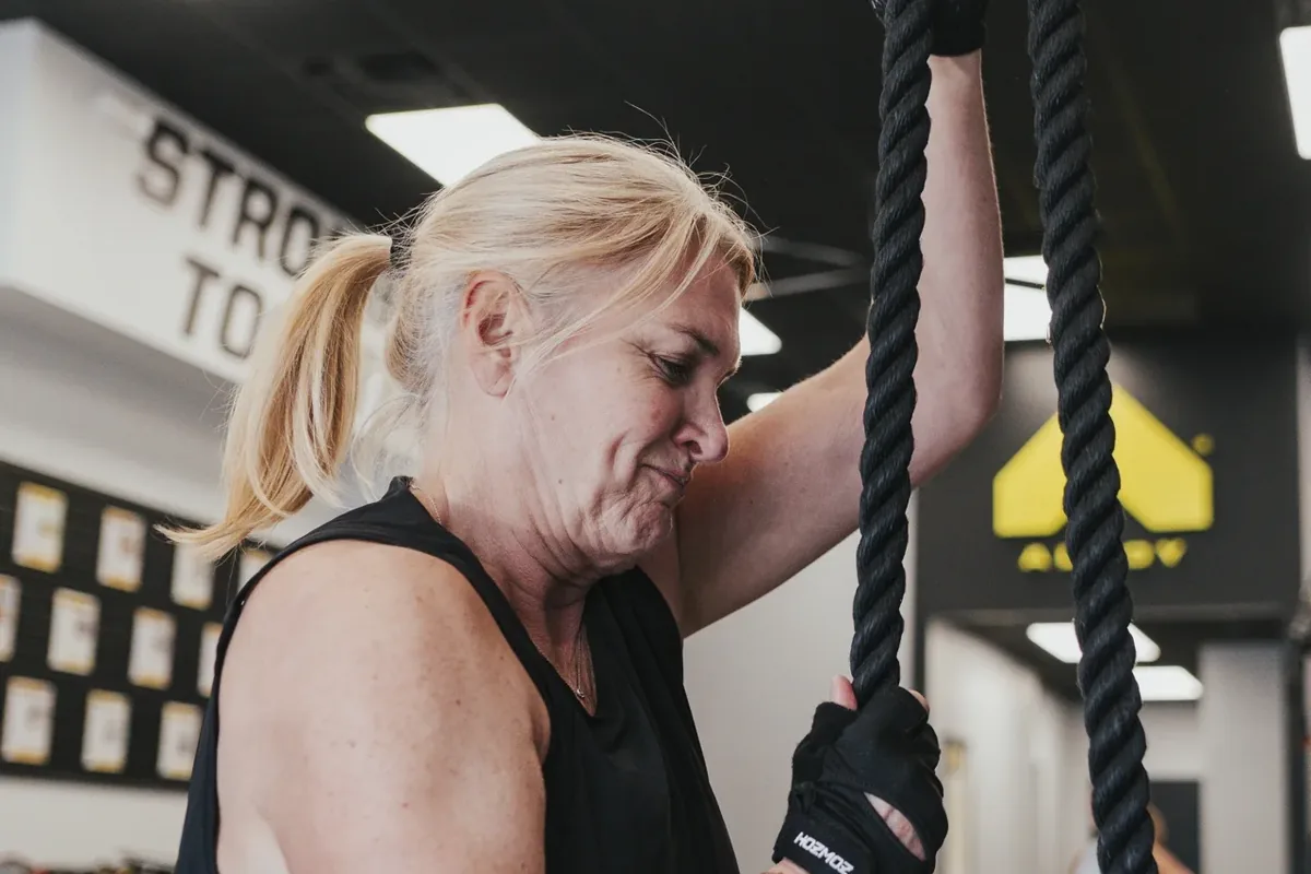 An older woman grips a heavy climbing rope mid-exercise