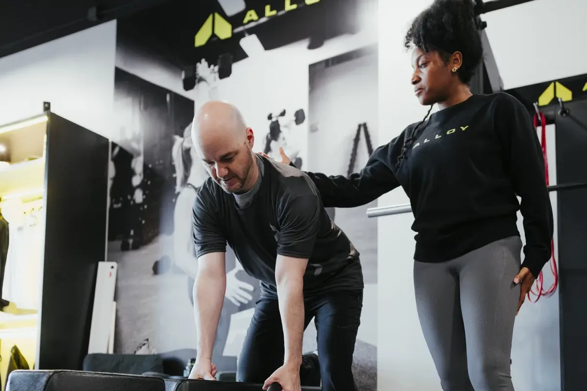 A coach steadies a member's arm during a supported dumbbell row on a bench
