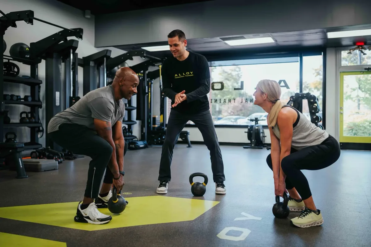 Coach cueing two members through side-by-side kettlebell squats on the Alloy studio floor