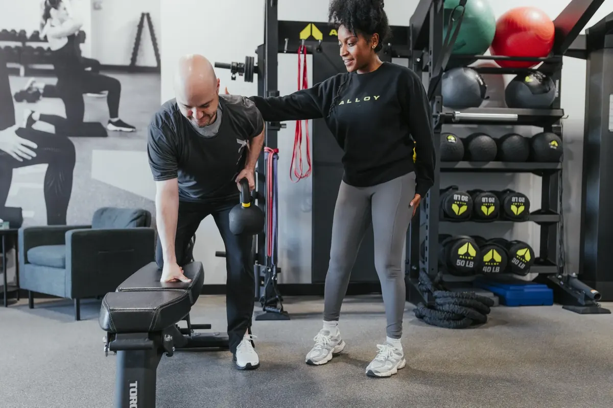 Coach cueing a member's upper-back position during a bench-supported kettlebell row at Alloy Madison East