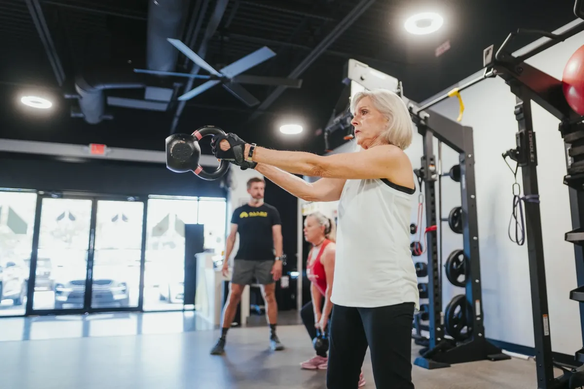Older woman performing a kettlebell swing during a coached session at Alloy Personal Training Madison East
