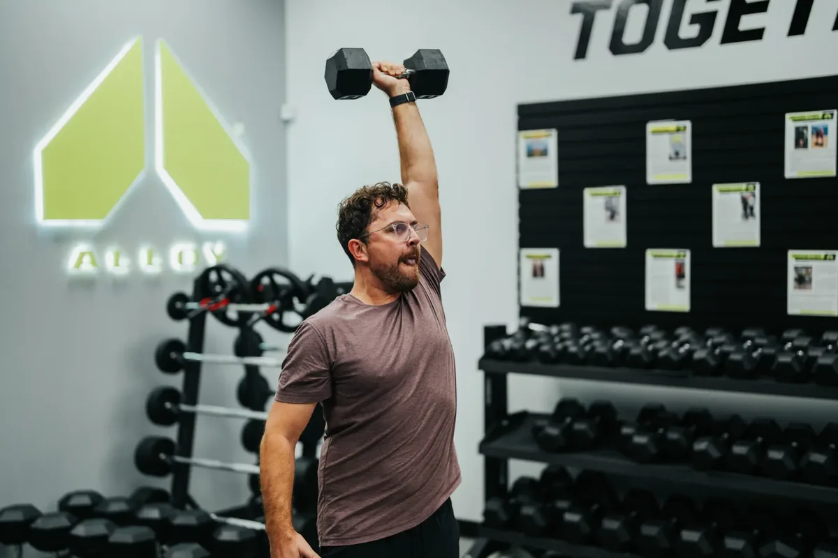 Man pressing a dumbbell overhead during a strength session at Alloy Personal Training Madison East