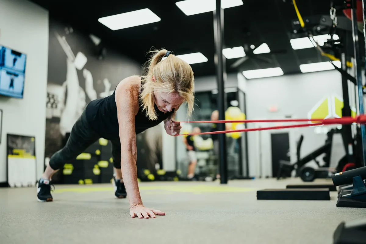 A woman holds a push-up plank with a resistance band across her back