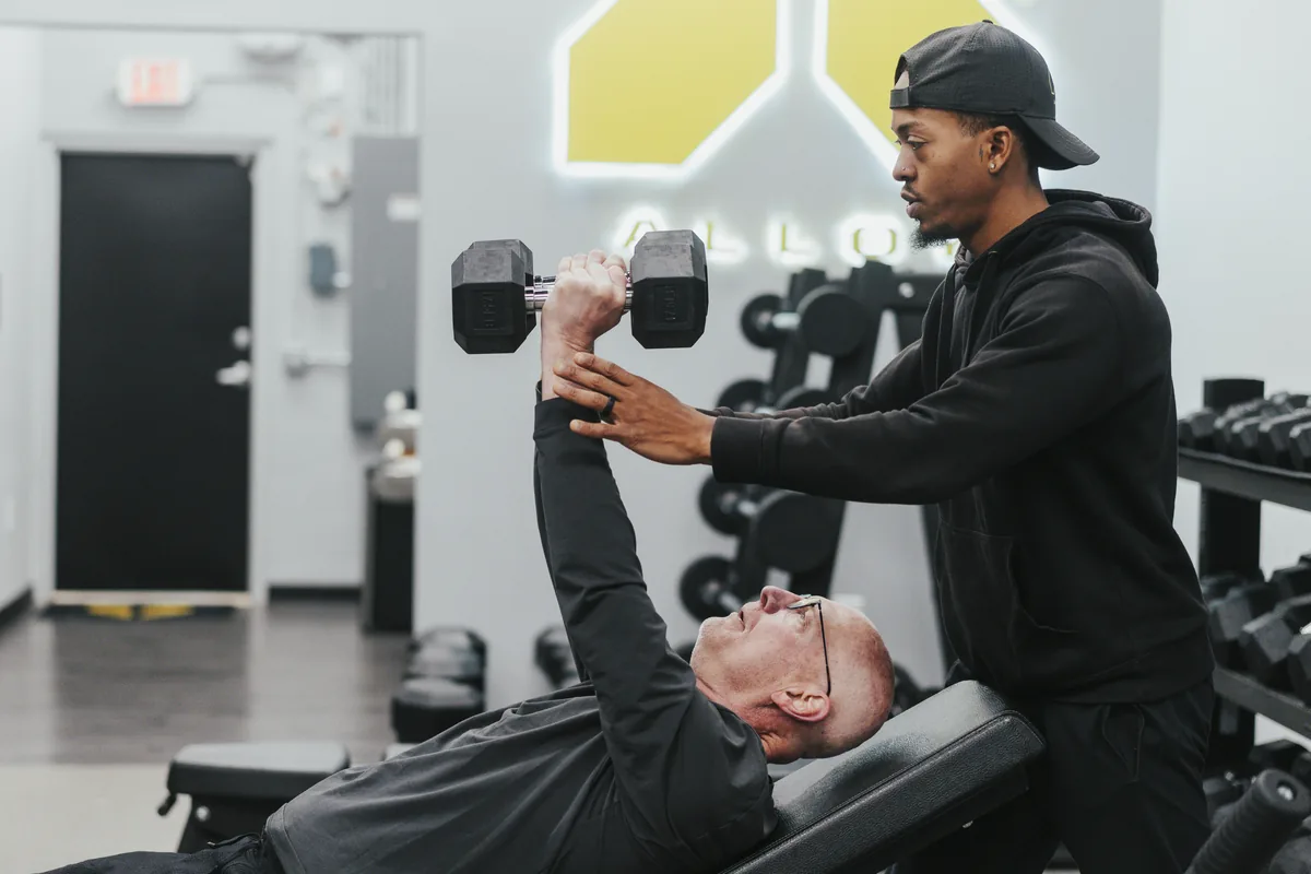 An Alloy coach spotting a member during a dumbbell bench press