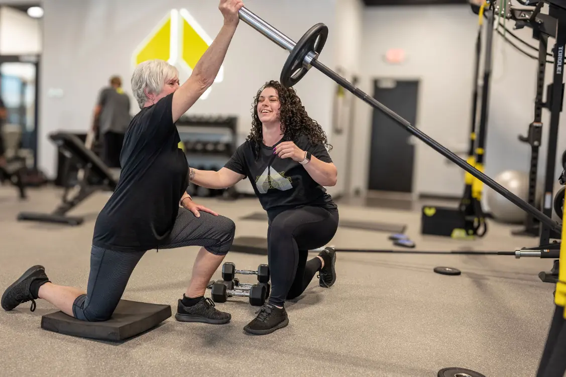 An Alloy coach guiding a member through a barbell press