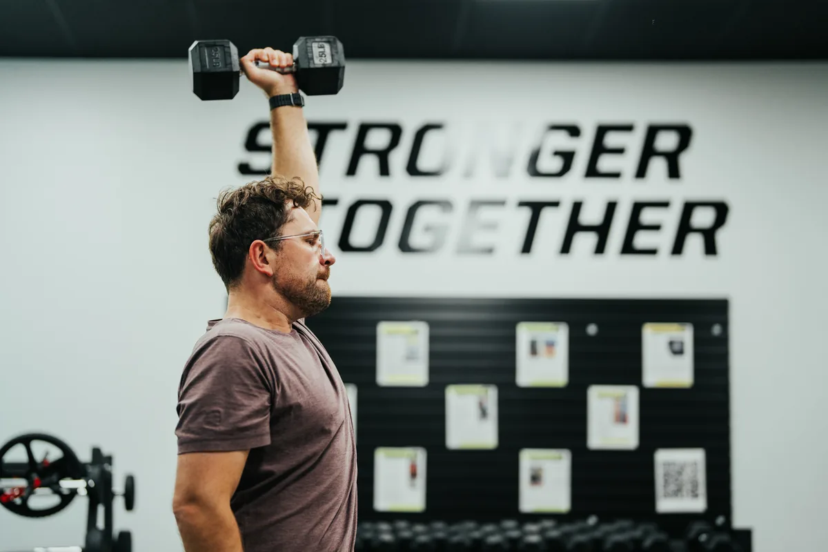 A member performing a standing dumbbell shoulder press at Alloy Madison East